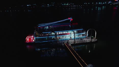 aerial flight towards blue and red lighting restaurant boat ready for departure at night