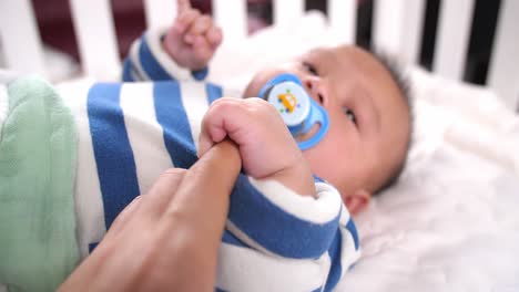 baby with a pacifier holding mother's finger, video in 4k