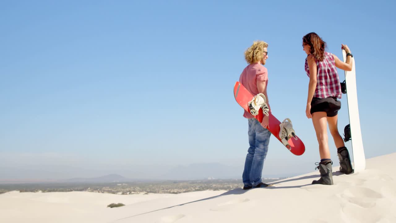 사막 4k에서 모래 보드와 함께 서 있는 커플