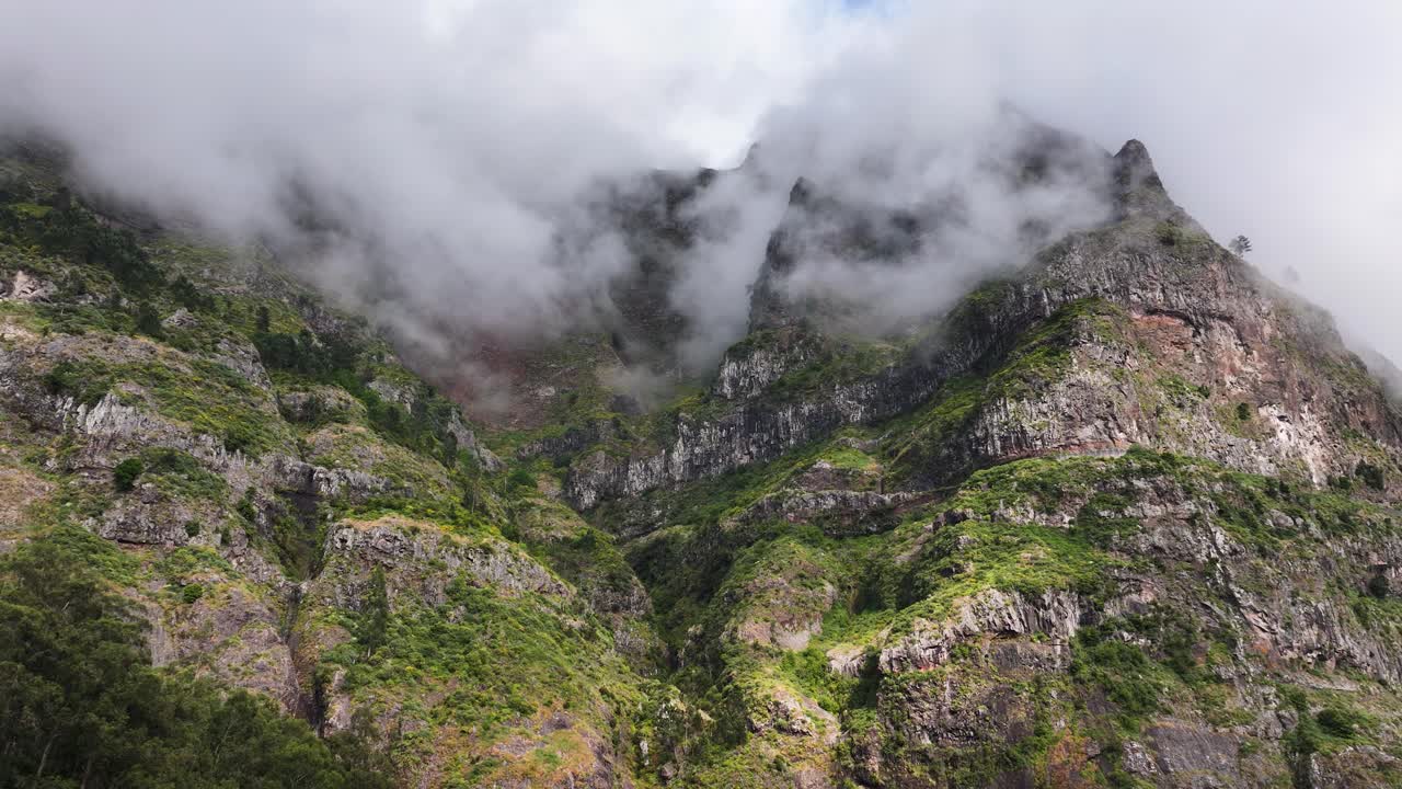 Imposing mountains with mountain fog surround Curral das Freiras parish, drone