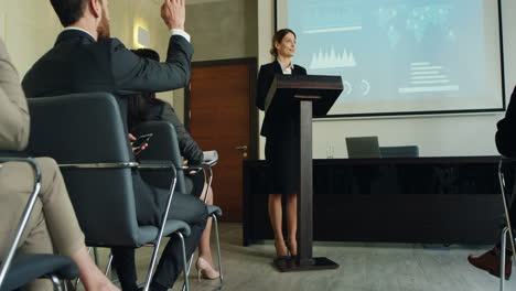zoom de cámara sobre una mujer de negocios caucásica hablando en un podio en una sala de conferencias y mostrando algunos gráficos y gráficos en la pantalla grande