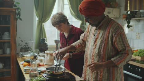 senior indian chef teaching young woman to cook flatbread in kitchen