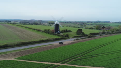 Toma-Aérea-De-Drones-Del-Antiguo-Molino-De-Viento-Rural-Del-Siglo-XIX-Catalogado-Como-Grado-Ii-Y-Campos-Verdes-Con-El-Viejo-Defensor-De-Landrover-Estacionado-Al-Costado-De-La-Carretera-Burnham-Overy-Staithe-North-Norfolk-Uk