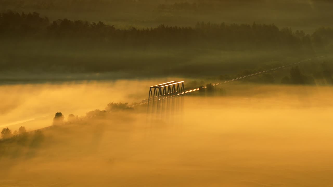 Aerial orbit over old railway bridge at sunrise with fog and warm light