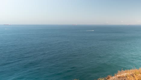 Océano-Azul-Con-Barcos-Y-Faro-En-Acantilados-Rocosos,-Vista-Panorámica-De-Lapso-De-Tiempo