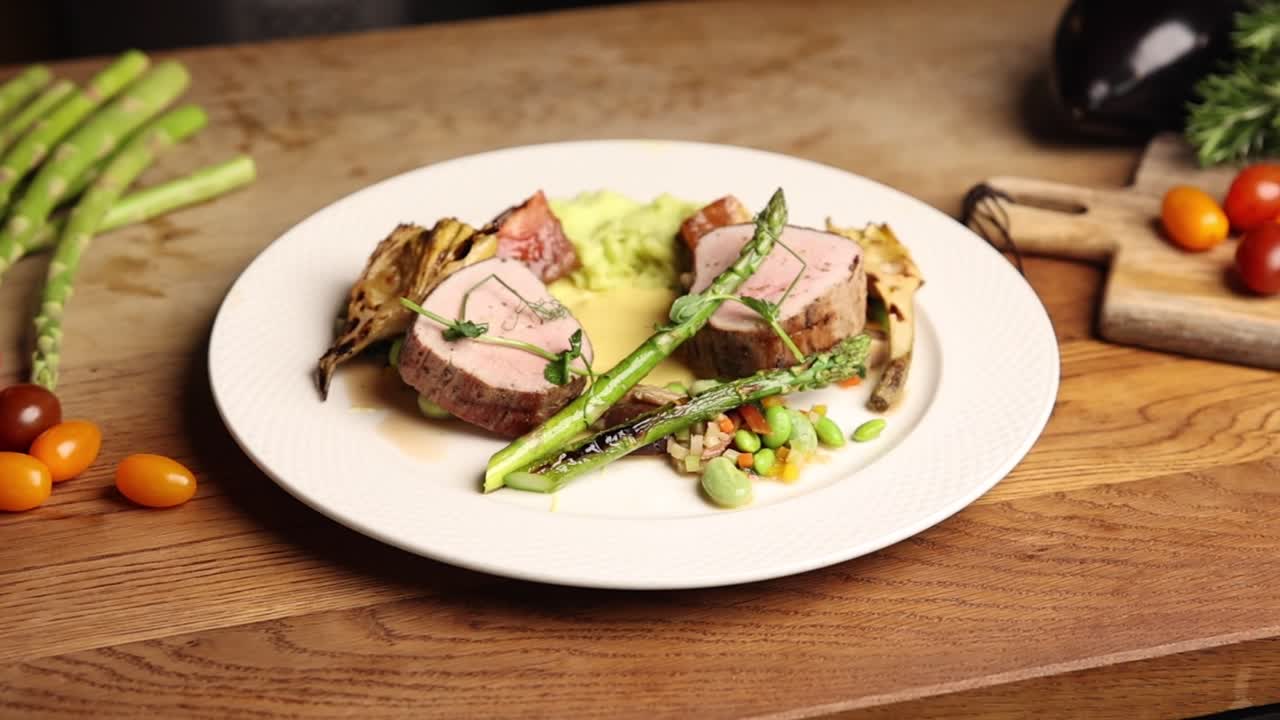 Presentazione gourmet di filetto di maiale con asparagi e verdure fresche.