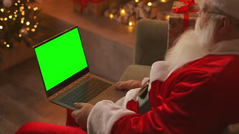 Papá-Noel-Está-Hablando-En-Una-Videollamada-A-Través-De-Una-Computadora-Portátil.-Utilice-La-Pantalla-Verde-Para-Una-Videollamada.-Papá-Noel-Saluda-Con-La-Mano-Mirando-La-Pantalla-Verde-Del-Portátil.-Imágenes-4k-De-Alta-Calidad