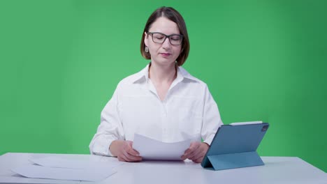 woman in glasses and white shirt leads a news release on the tv channel, green chromakey on background. blogger is streaming for her business vlog