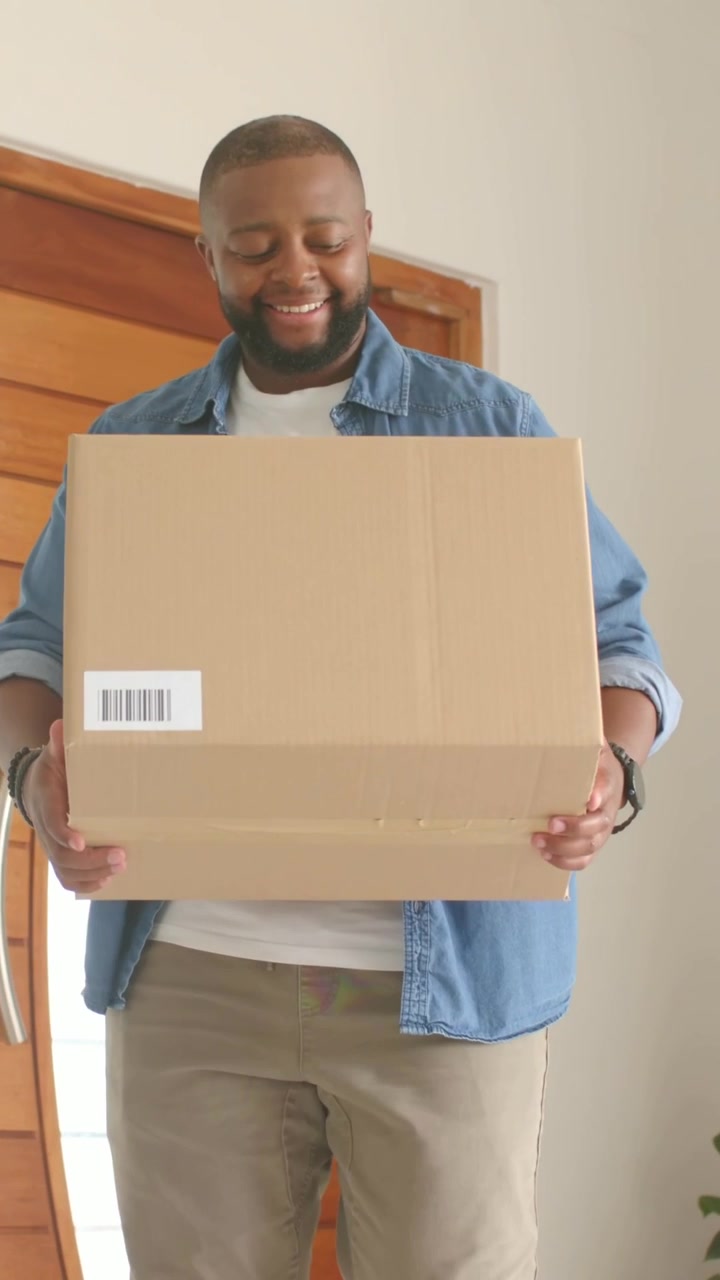Video vertical: Hombre caminando en casa sosteniendo una caja con etiqueta desde la puerta, metiéndola dentro
