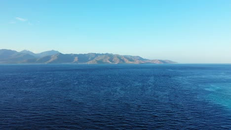 stunning scenery of blue calm ocean with mountain background clear blue sky above - aerial shot