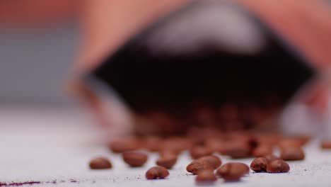 Falling-coffee-bag-in-blurred-background-with-rolling-roasted-coffee-beans-on-table-in-focus