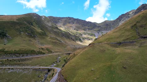 Drone-descends-along-hillside-as-car-drive-along-Transfagarasan-Serpentine-Road-at-midday