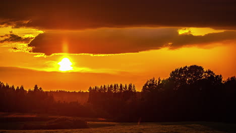 Bright-orange-sunset-glowing-above-the-summer,-green-countryside---time-lapse-cloudscape