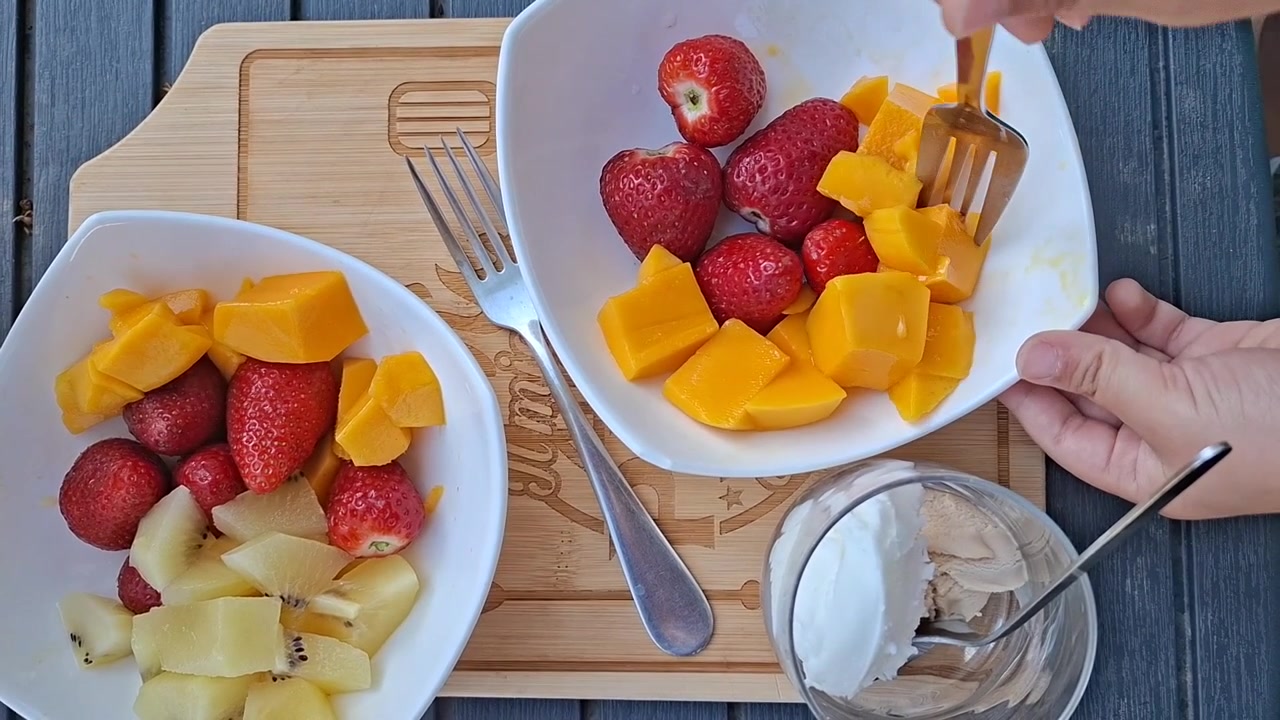 Bambino che prende una fetta di mango scivolosa con la forchetta dalla ciotola di frutta, vista dall'alto.