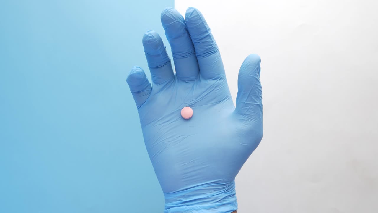 mano con guantes azules sosteniendo una píldora rosa