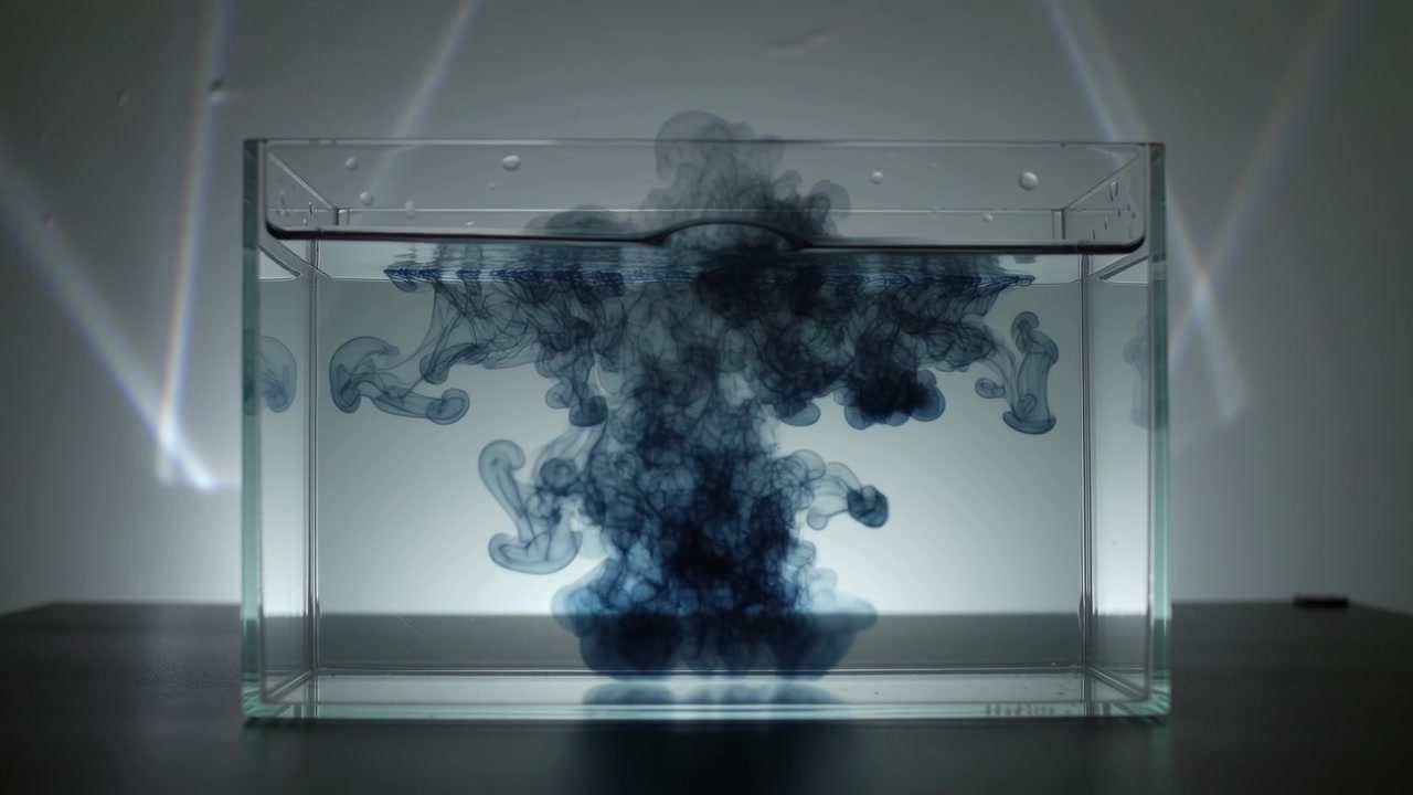 Dropper releasing dark blue ink into glass aquarium on tabletop, showing diffusion as plume forming
