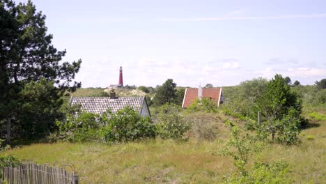 wide shot moving up from the ground to reveal dune landscape with red lighthouse on schiermonnikoog island, the netherlands