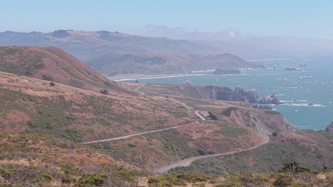 Coastal footage reveals the dynamic textures of ocean, rock, and hillside meeting under the afternoon sun