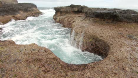 a surge of ocean water as it pushes up into a hole in the rock shelf and crashes back down