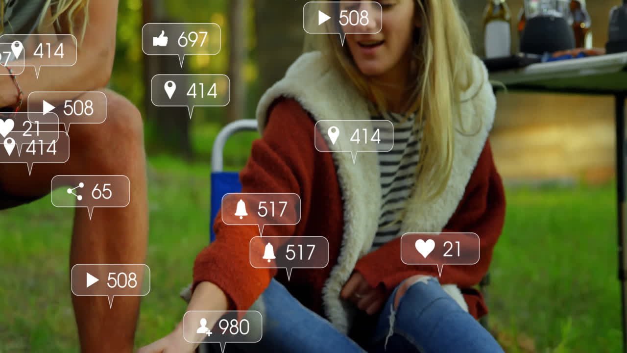 Campers warming hands by campfire in forest clearing, featuring floating social media icons