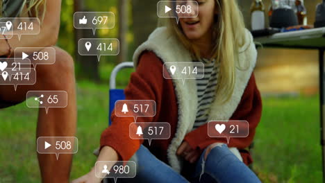 campers warming hands by campfire in forest clearing, featuring floating social media icons