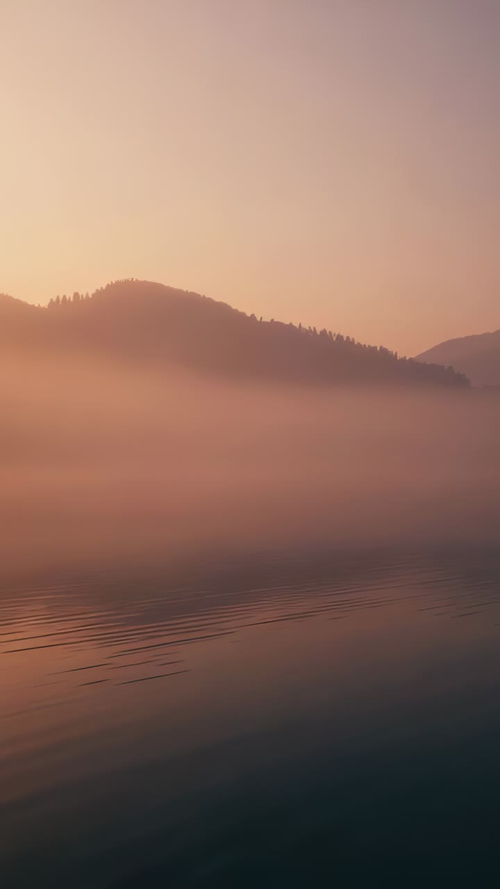 Vertical video: Drifting mist and ridge shifting at mountain lake as sky brightens, rippling water