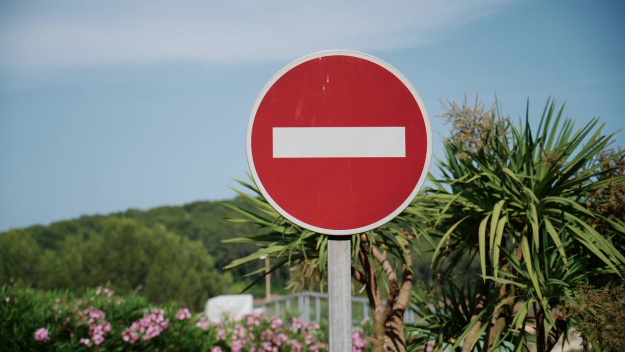 Red no entry traffic sign standing against a sunny natural background with greenery and blue sky