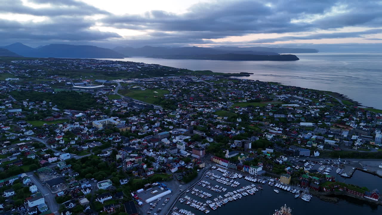 Cinematic aerial view of torshavn harbor in faroe islands with fishing boats, colorful houses, shipping port and dramatic coastline under soft evening light