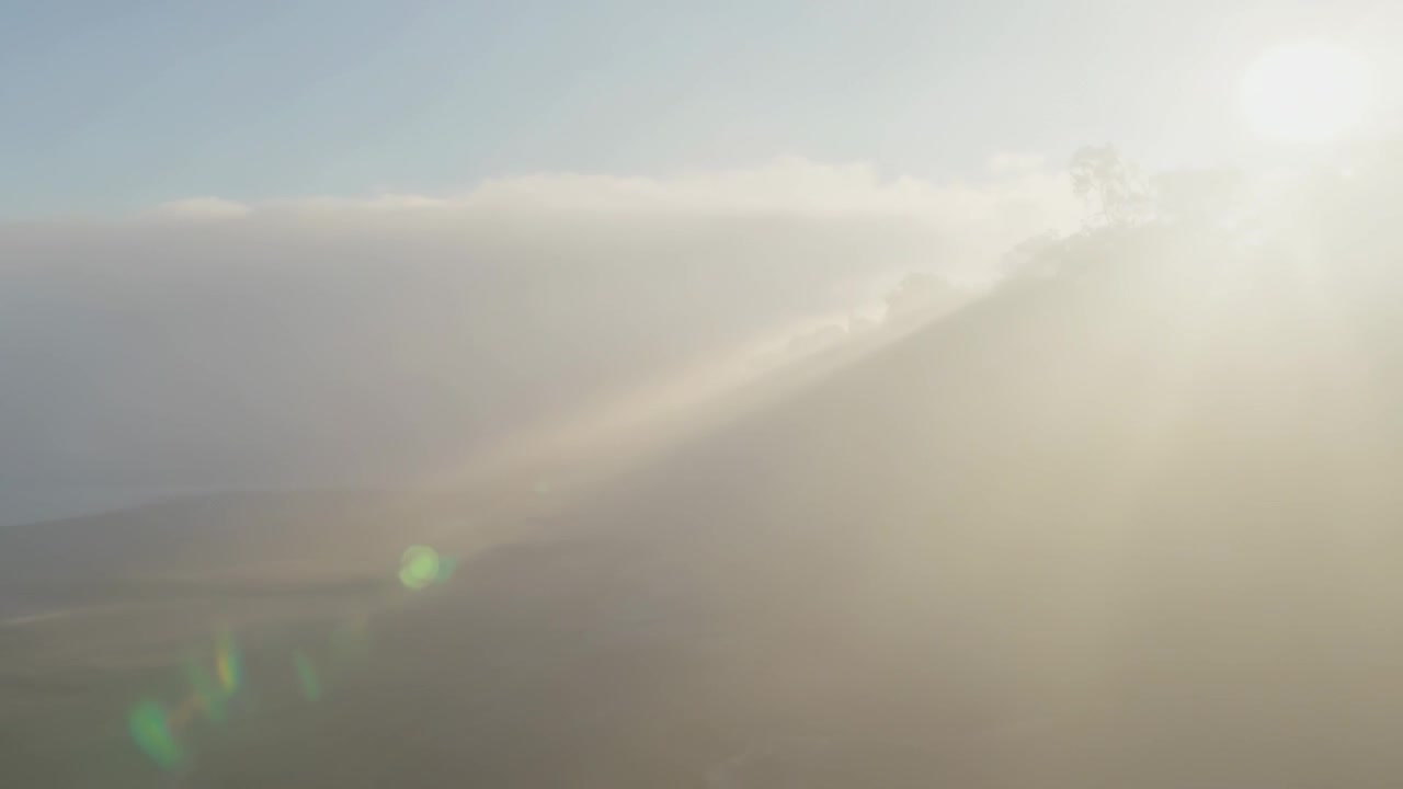 Brightening sun sending rays across foggy valley, revealing ridge outline and creating green flares