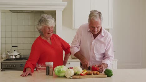 caucasian senior couple chopping vegetables together in the kitchen at home