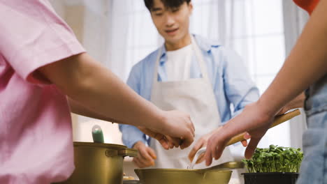 vista inferior de tres amigos japoneses vertiendo ingredientes en la sartén mientras cocinan en la cocina