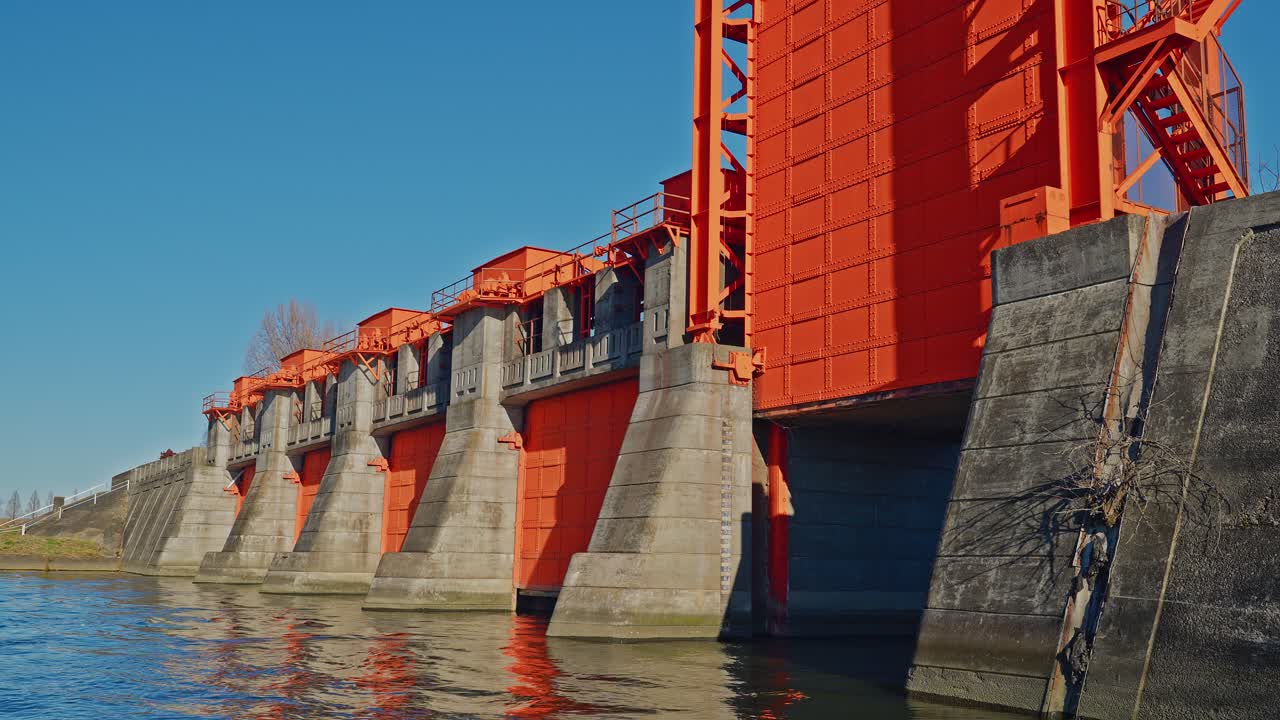 A powerful perspective shot from the water level, showcasing the massive concrete piers and weathered red steel gates of the historic Iwabuchi Sluice