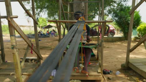 joven trabajador africano tejiendo textil de seda kente en un telar rudimentario