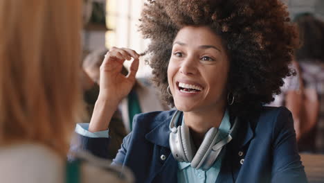 Hermosa-Mujer-De-Raza-Mixta-Con-Peinado-Afro-Charlando-Con-Un-Amigo-En-Un-Café-Bebiendo-Café-Socializando-Disfrutando-De-Una-Conversación-En-Un-Concurrido-Restaurante