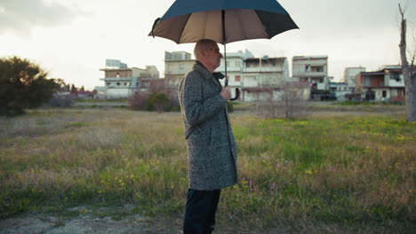 senior man in the park starts to feel raindrops and opens the umbrella