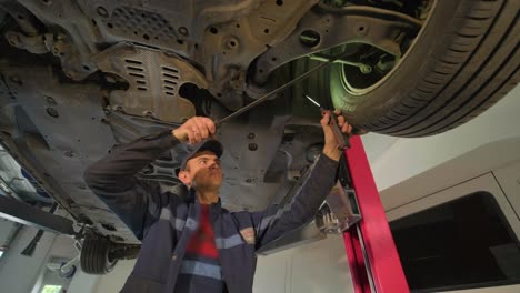 young car mechanic at repair service station inspecting car wheel and suspension detail of lifted automobile. bottom view.
