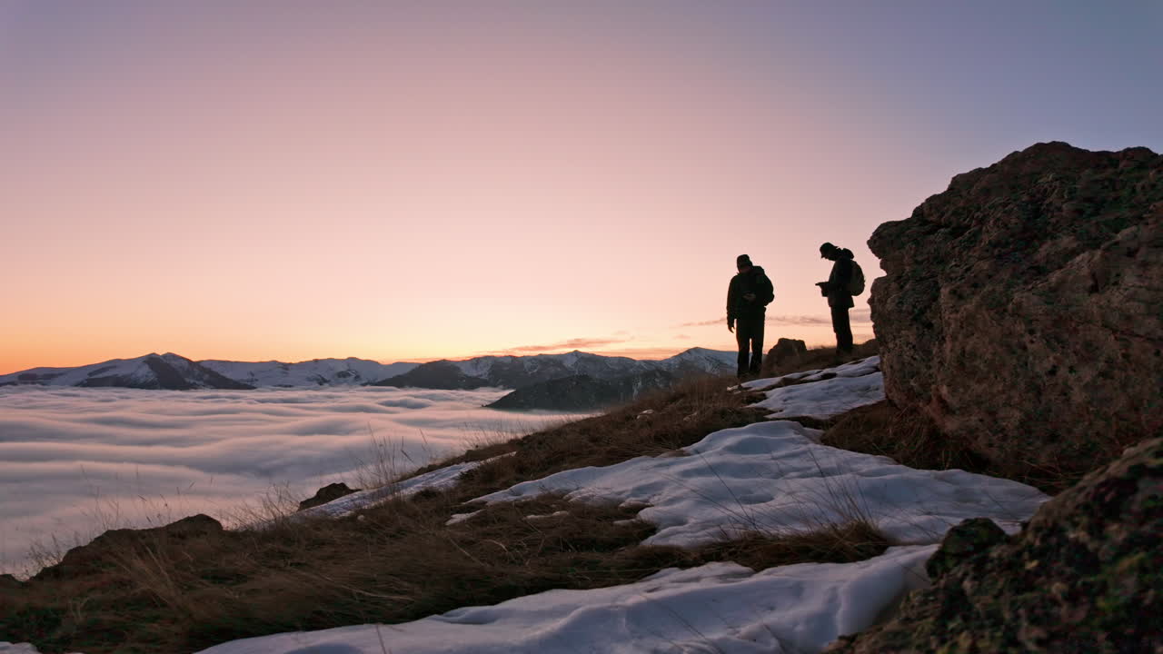 Escursionisti si godono una scenografica alba sopra le nuvole durante un'escursione in montagna innevata.