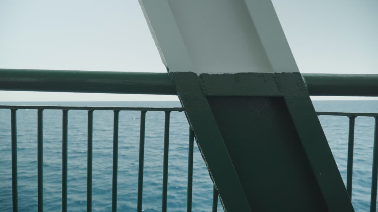 Schiffsreling mit Blick auf den ruhigen Ozeanhorizont, diagonaler Stützbalken rahmt das ferne Wasser ein, sanftes türkisfarbenes Licht, sanfte Wellen, minimale industrielle Textur, Ruhe des offenen Himmels, filmische Komposition.