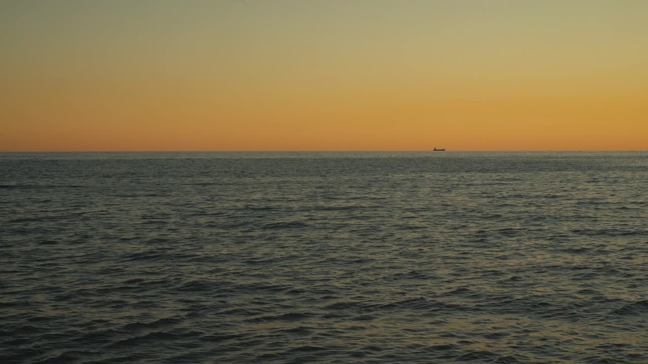 Small fishing boat sails away on a calm sea, surrounded by a stunning sunset that paints the sky in vibrant colors