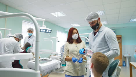 medical student holding dental model of a set of teeth in front of patient. male student shows how to clean teeth correctly and teacher comes to check his work.