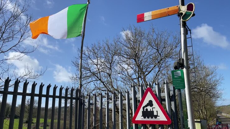 Bandiera irlandese, vecchio segnale ferroviario e cartello del treno e cielo blu alla stazione di Kilmeaden, Waterford, Irlanda