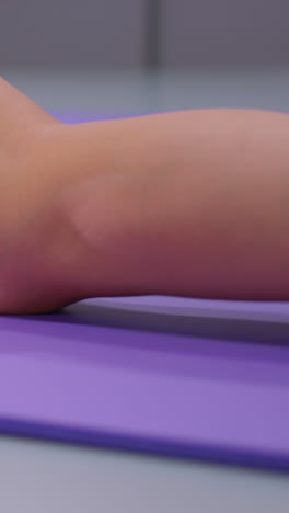 primer plano de estiramiento de piernas realizado en una alfombra de yoga púrpura, mostrando pierna y pie en calcetines blancos, enfatizando el detalle y la tensión durante una sesión de entrenamiento