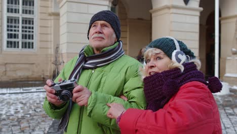 Senior-couple-tourists-grandmother-grandfather-taking-photo-pictures-on-retro-camera-in-winter-city