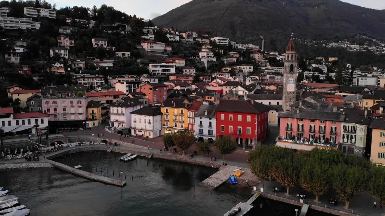 sobrevuelo aéreo a lo largo del paseo junto al lago de ascona, ticino a orillas del lago maggiore en la suiza italiana al final de un día de verano con casas coloridas, torre de la iglesia y embarcadero a la vista