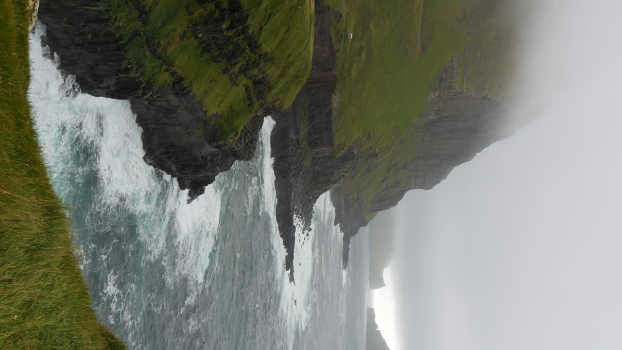Vertical shot of waves crashing on cliff on foggy day, Faroe Islands