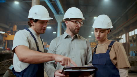 two industrial workers discussing documents with engineer in factory