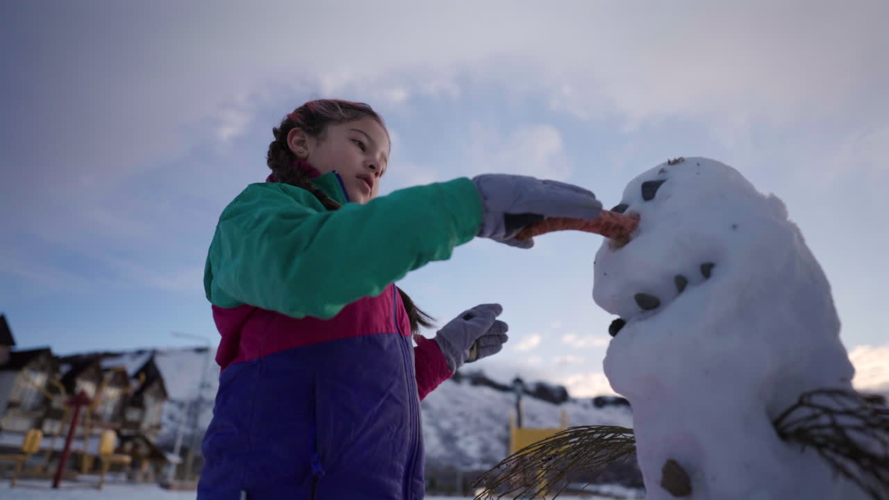 Close-up of Hispanic girl building snowman outdoors during winter holiday in scenic town