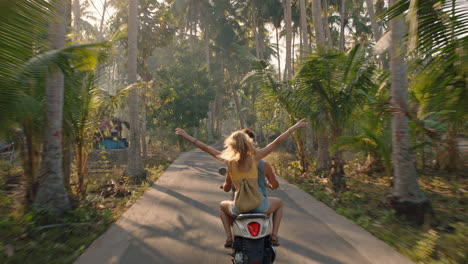 pareja feliz montando un scooter en una isla tropical novia divirtiéndose con los brazos levantados explorando un hermoso destino de viaje en motocicleta con su novio