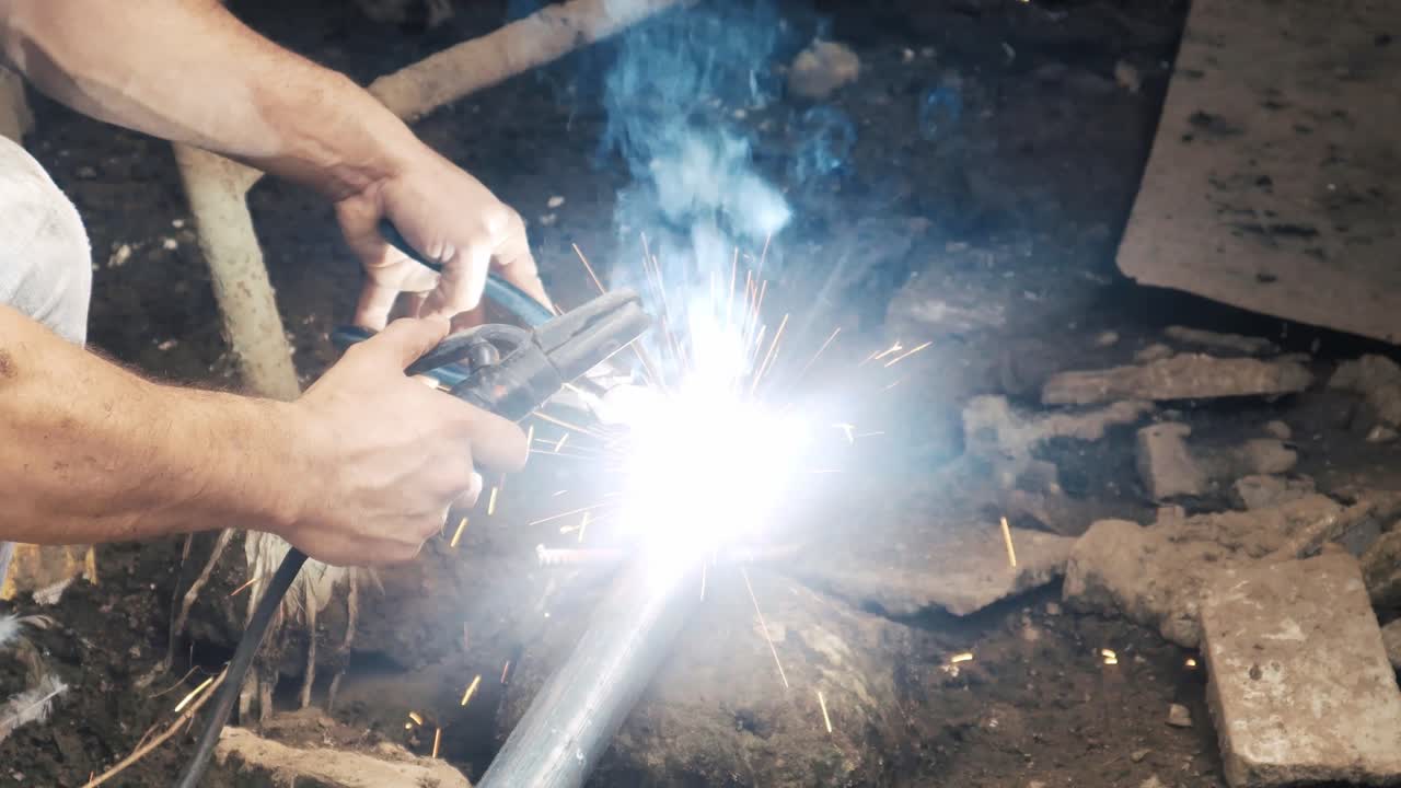 Professional welder employing industrial welding machine to put together two pieces of metal creating a metalic structure as part of his daily work at a local small business