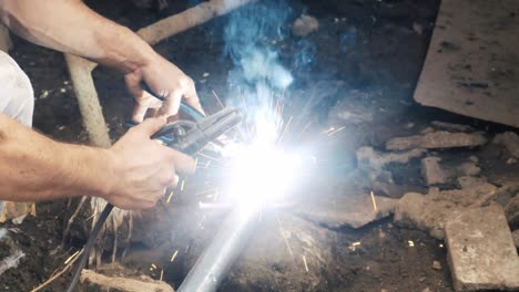 professional welder employing industrial welding machine to put together two pieces of metal creating a metalic structure as part of his daily work at a local small business